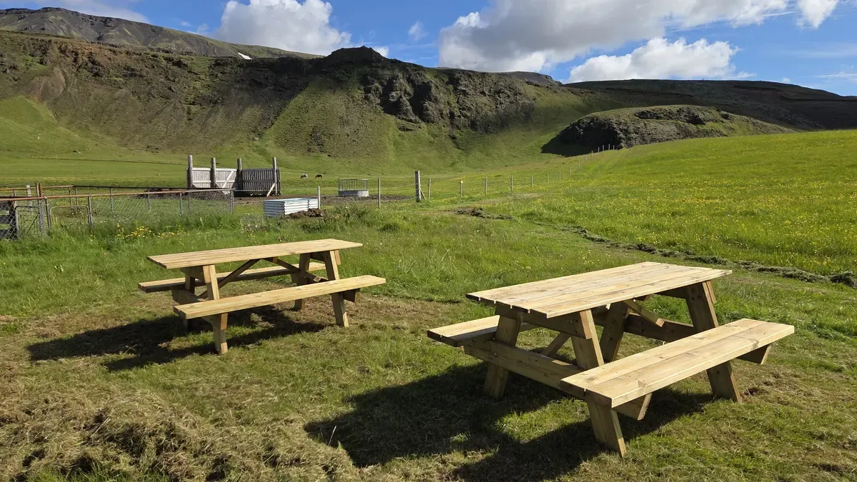 Wooden picnic tables in the green fields beneath the Eyvindarholt hills