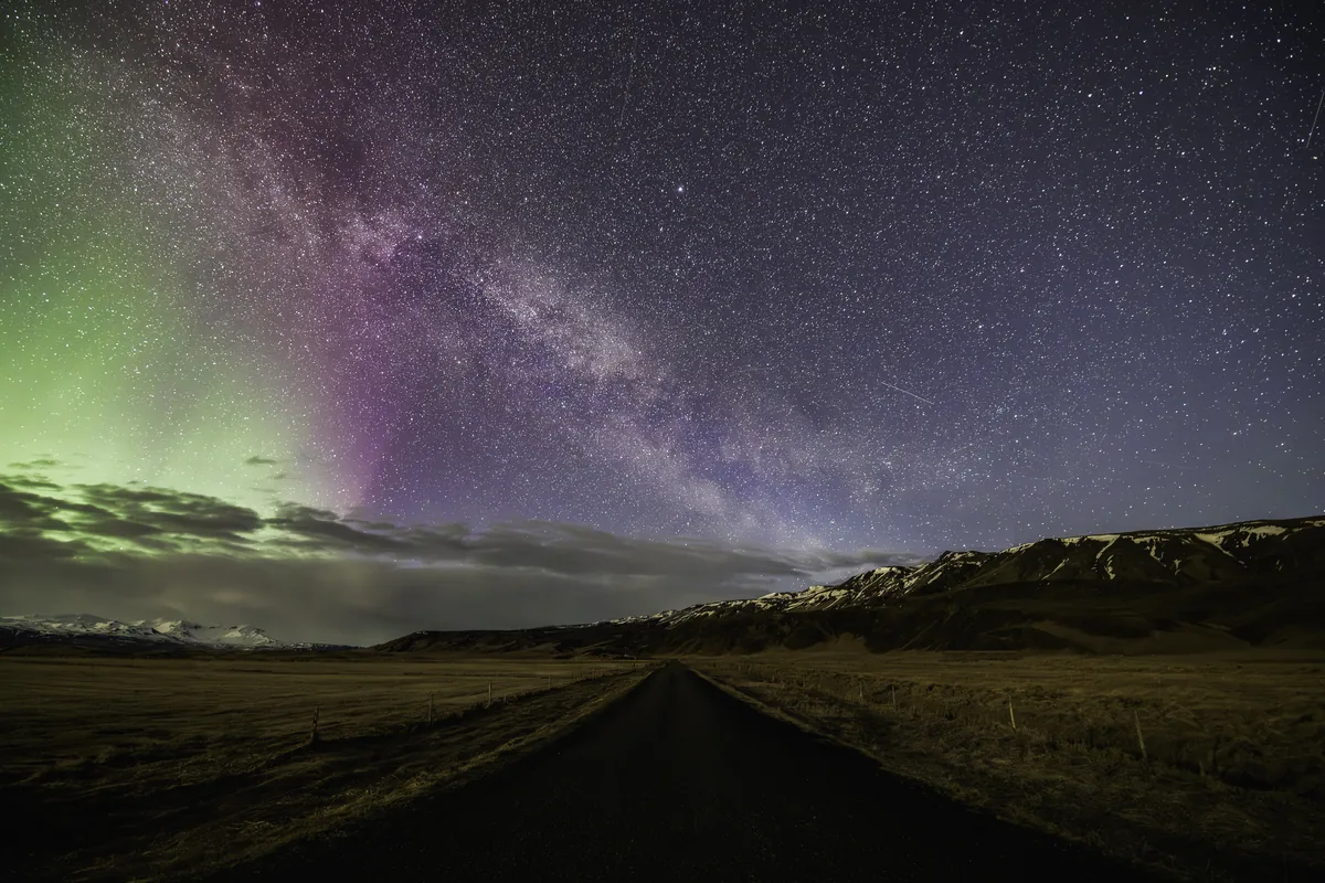 A quiet road and mountains beneath stars and northern lights
