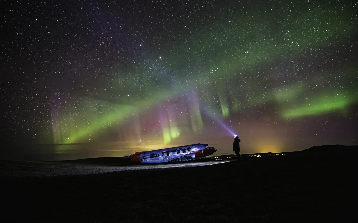 Green and purple northern lights above the DC-3 and a visitor at Eyvindarholt