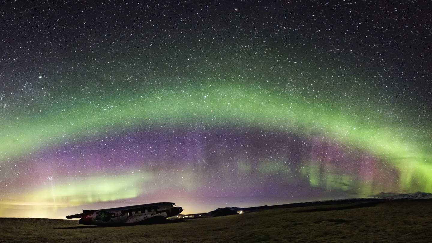 An arch of green and purple northern lights above the DC-3